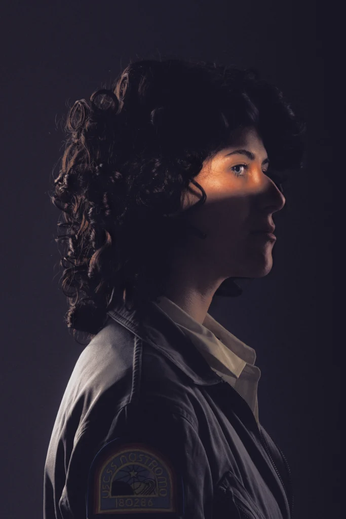 Ellen Ripley cosplayer from the movie Alien posing in dramatic and ominous lighting looking into the distance.