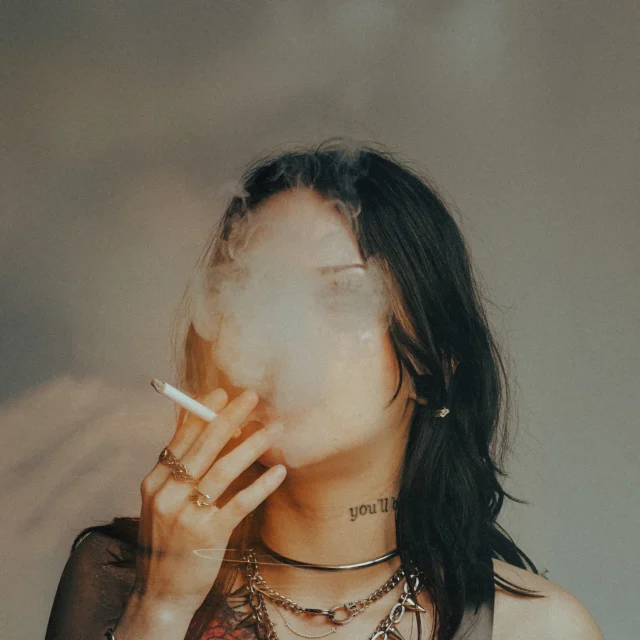 Gothic fashion model in gothic apparel smoking cigarette with smoke covering face industrial editorial portrait