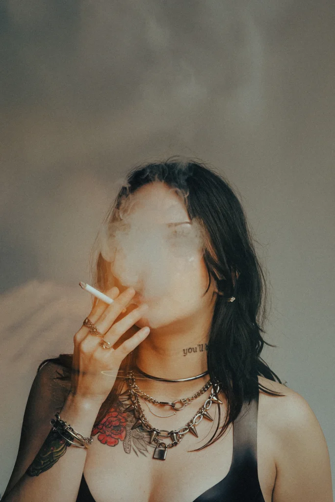 Gothic fashion model in gothic apparel smoking cigarette with smoke covering face industrial editorial portrait