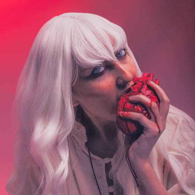 Griffith from Berserk cosplayer with long white hair eating a fake heart in editorial fantasy portrait