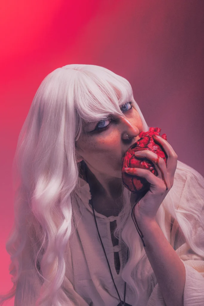 Griffith from Berserk cosplayer with long white hair eating a fake heart in editorial fantasy portrait